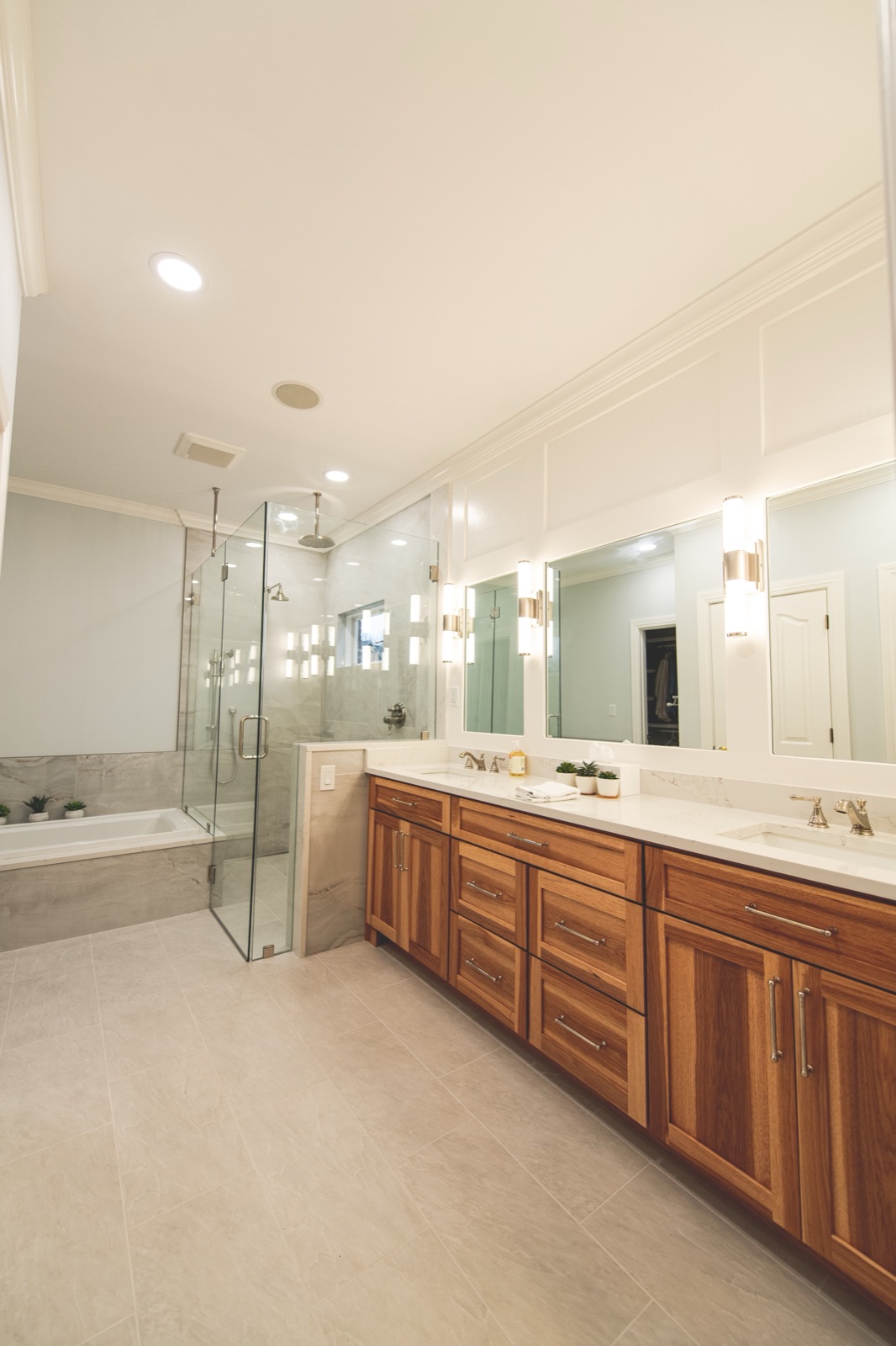 Walnut vanity with sconces, large mirrors, walk-in glass shower
